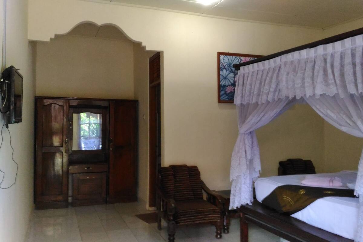 A bedroom with a four-poster bed, a wooden wardrobe, a chair, and a painting on the wall.