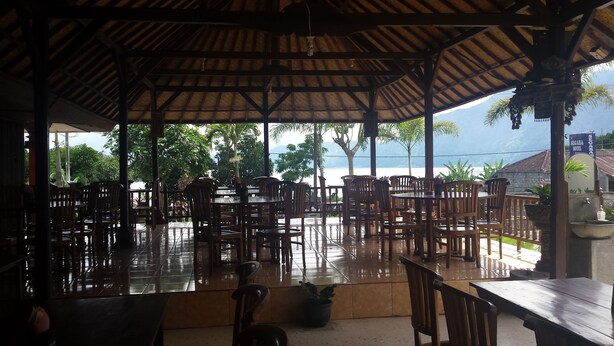 An outdoor seating area with wooden tables and chairs, a tiled floor, and a view of the sea and mountains. - Segara Hotel and Restaurant (Kintamani)