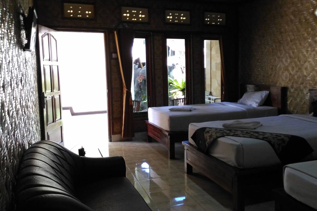 A hotel room with two beds, a sofa, and a large window with curtains.