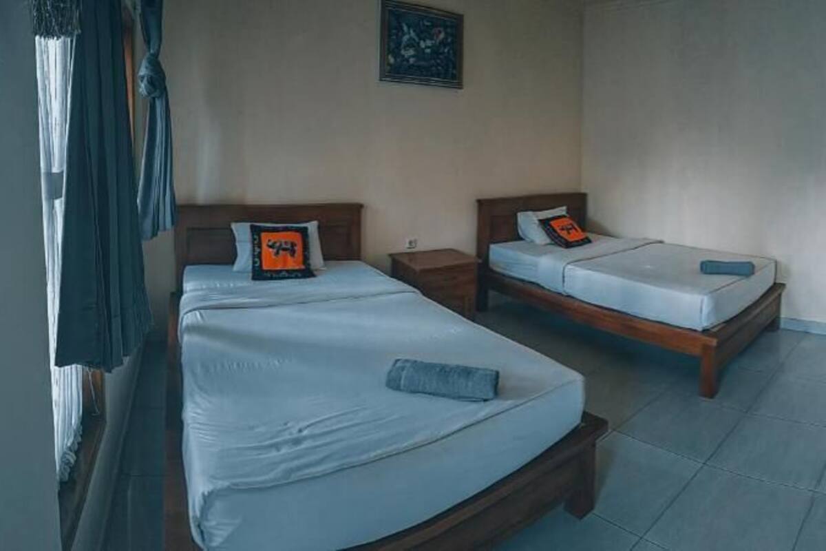 A hotel room with two single beds, a desk, a chair, and a television on the wall.