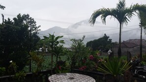 A garden with a tiled table, various plants, and a view of mountains in the background. - Segara Hotel and Restaurant (Kintamani)