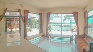 A room with large windows, a wooden bench, and a view of a beach and palm trees. - Segara Hotel and Restaurant (Kintamani)