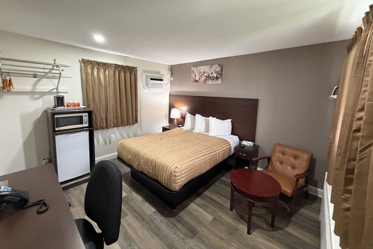 Une chambre d’hôtel comprenant un lit, un bureau avec un téléphone, une chaise, une petite table, un appareil de climatisation et une œuvre d’art accrochée au mur.