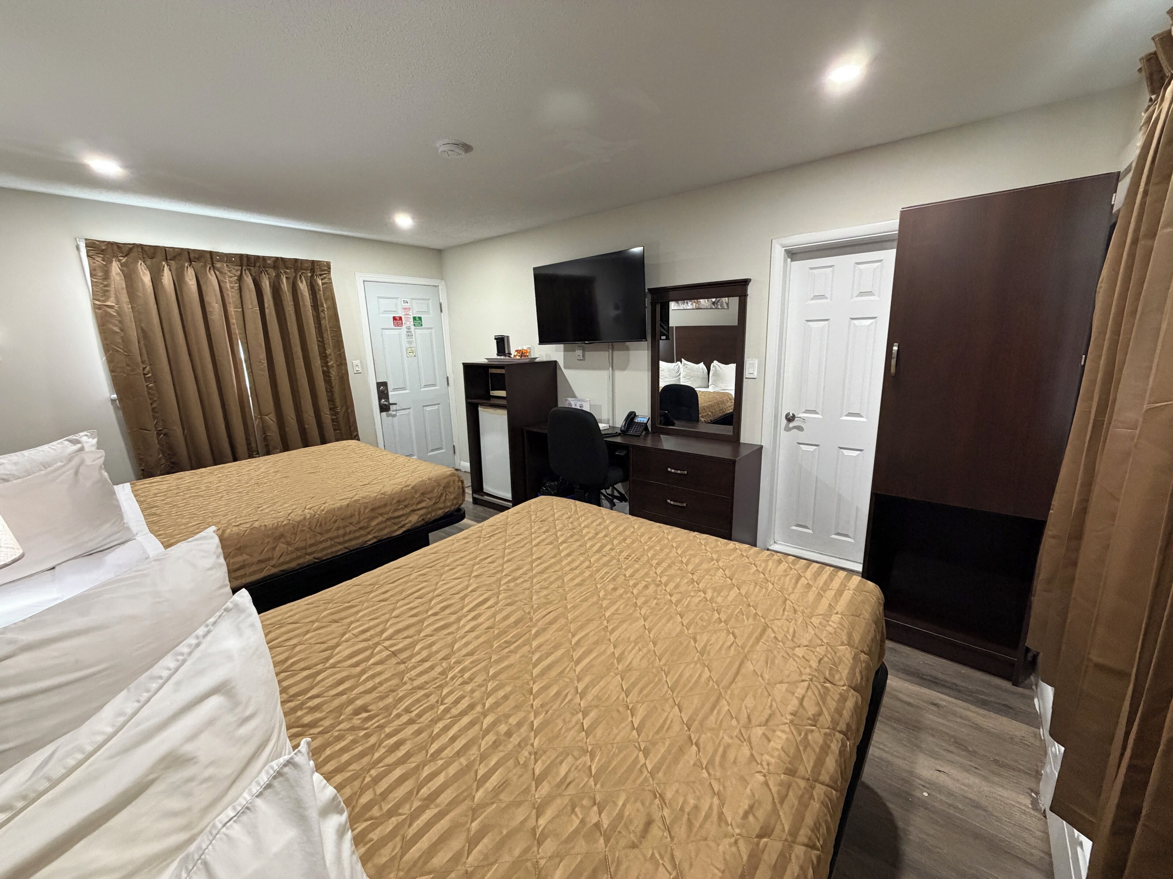 A hotel room with two beds, a desk, a mirror, a television, and a wardrobe.