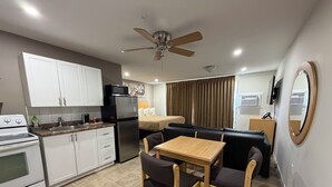 A compact kitchen with a stove, microwave, and refrigerator. There is a dining area with a table and chairs. A ceiling fan is visible, and the room has a neutral color scheme. - Perth Plaza Inn & Suites (Perth)