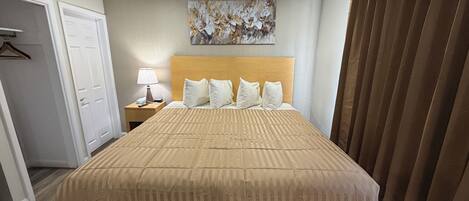 A hotel room with a large bed, a nightstand with a lamp, a painting on the wall, and a door.
