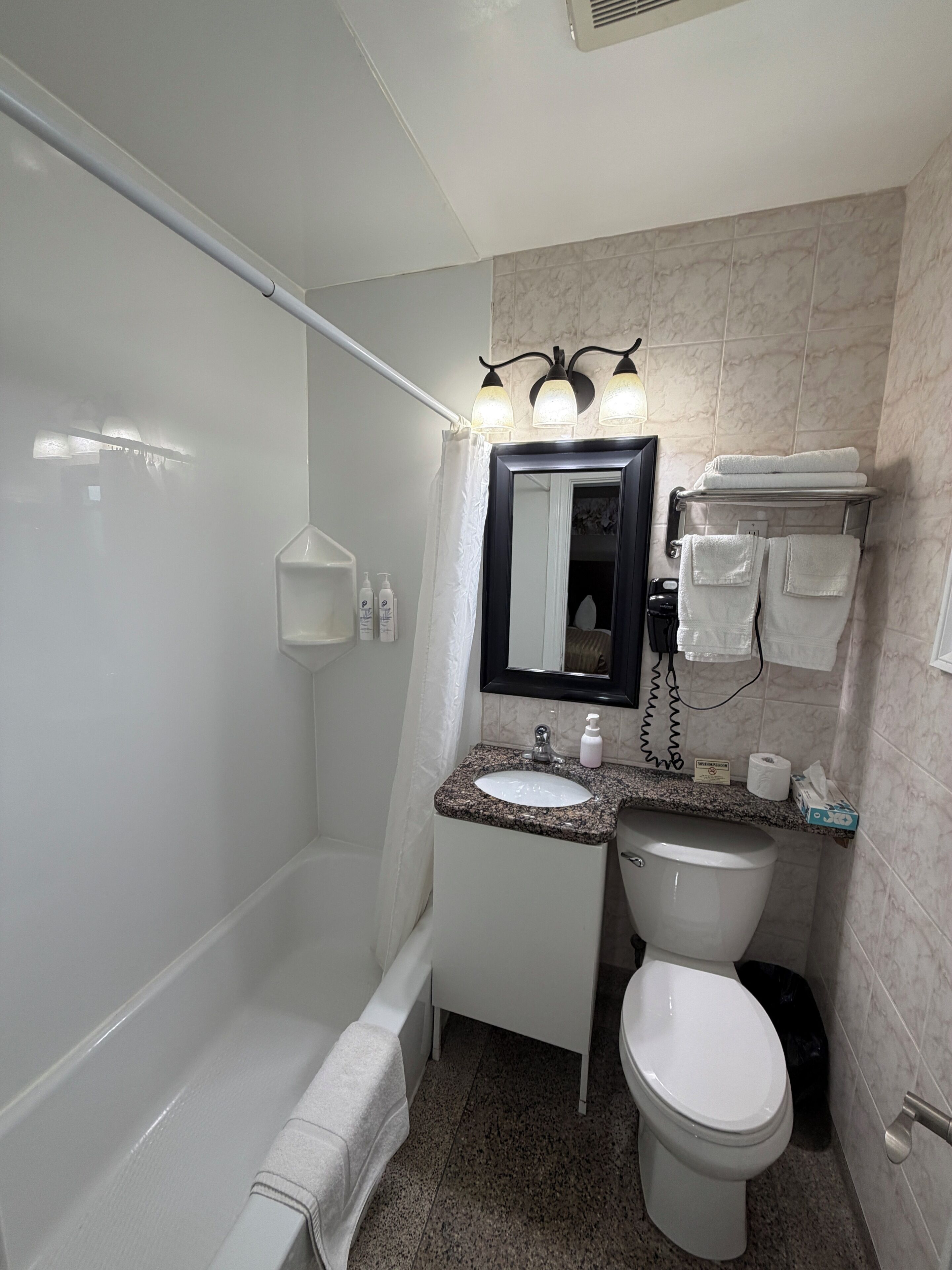 A bathroom with a bathtub, a sink, a toilet, and a mirror. There are towels and toiletries visible.