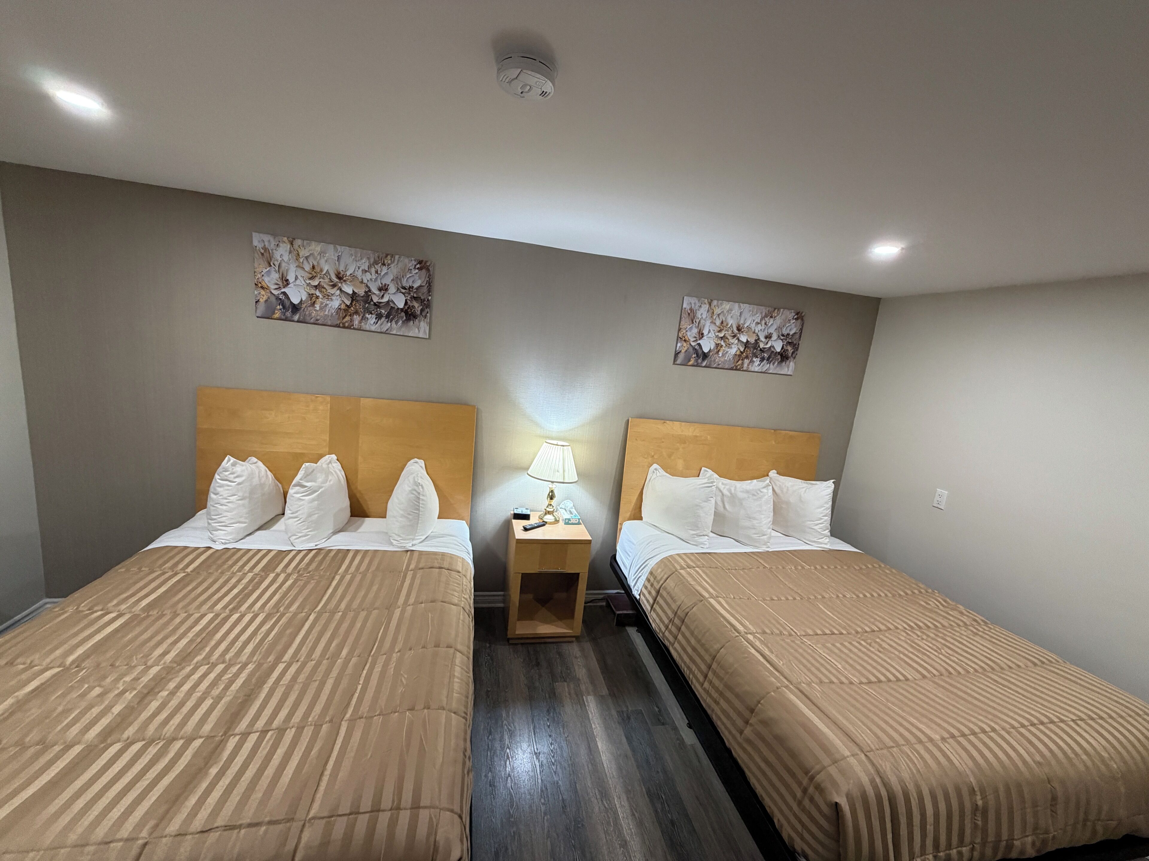 Une chambre d’hôtel avec deux lits, une table de chevet avec une lampe et deux œuvres d’art florales décorant le mur.