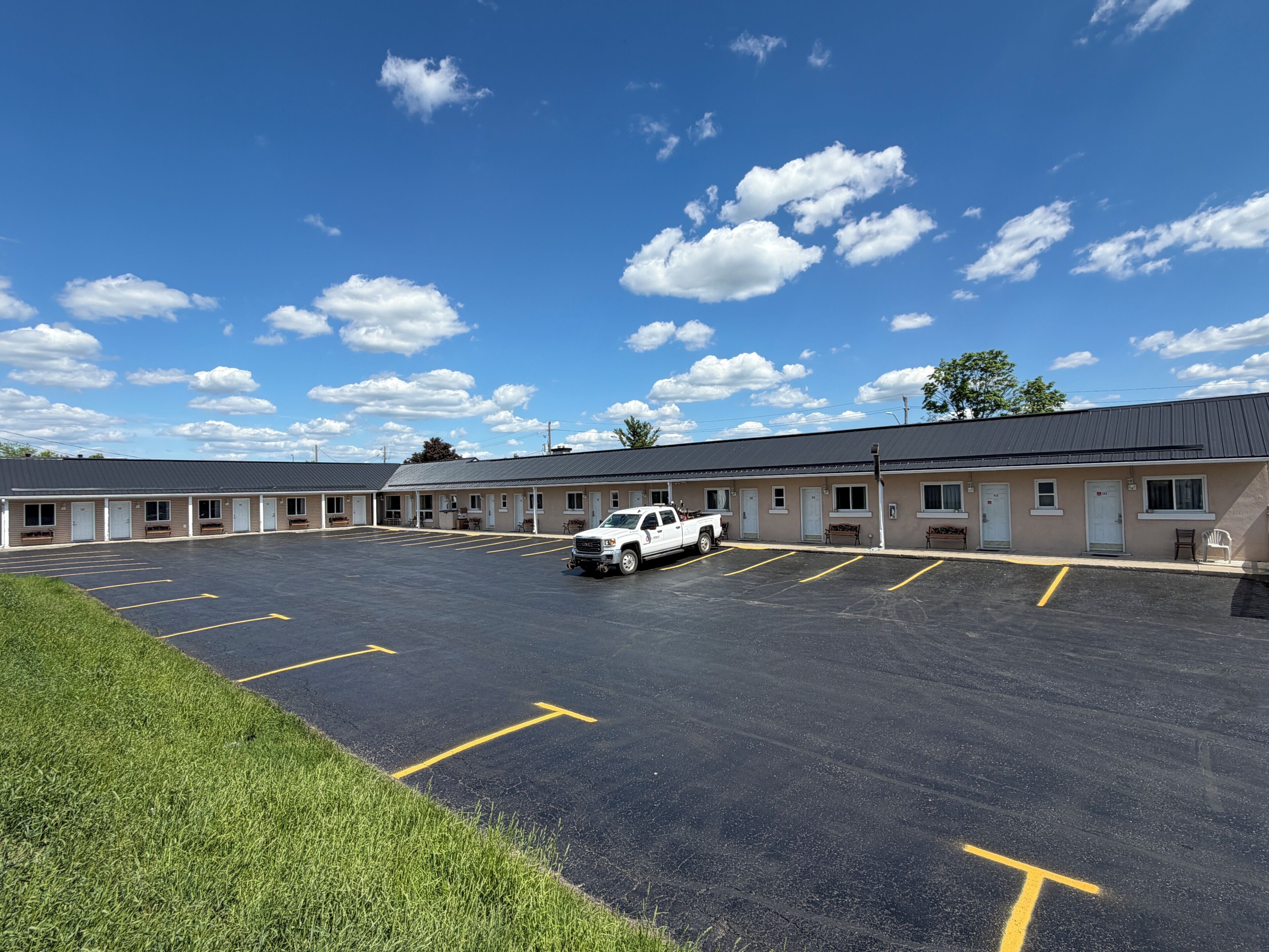 A motel with a parking lot, a white truck, and a clear blue sky.