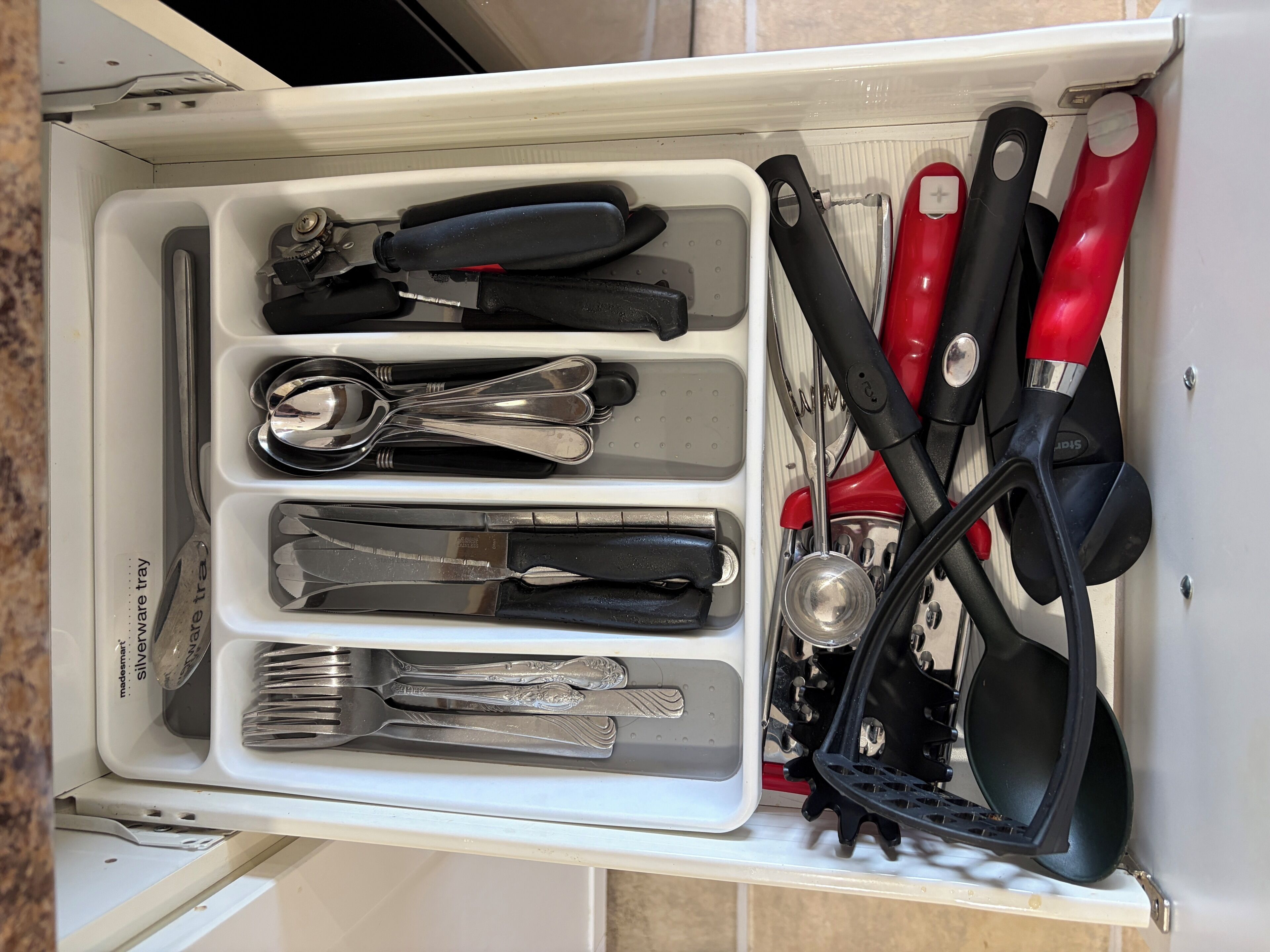 Uma gaveta com utensílios, incluindo garfos, facas e uma colher, dispostos em divisórias.