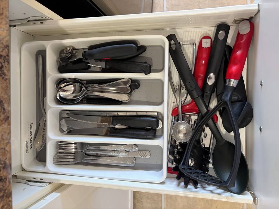 Uma gaveta com utensílios, incluindo garfos, facas e uma colher, dispostos em divisórias.