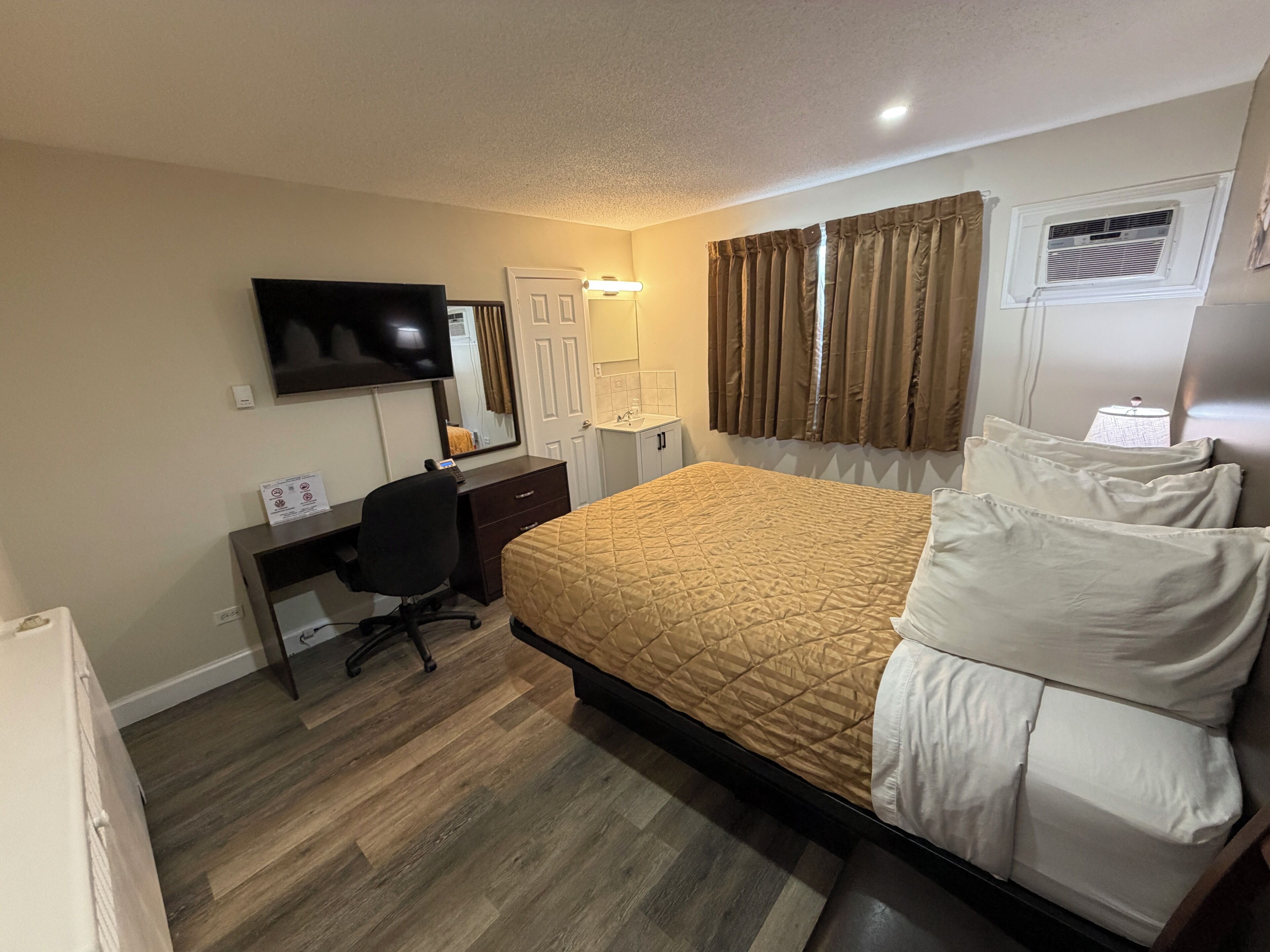 A hotel room with a bed, desk, chair, television, and a window with curtains.