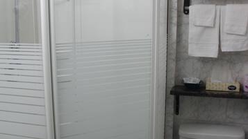 A bathroom with a glass-enclosed shower, a toilet, and a shelf with towels.
