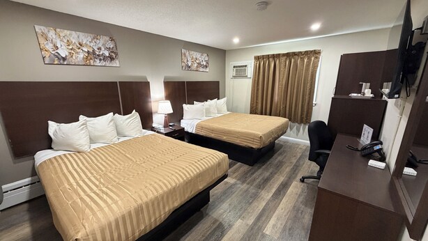 A hotel room with two beds, a desk, a chair, a TV, and artwork on the walls. - Perth Plaza Inn & Suites (Perth)