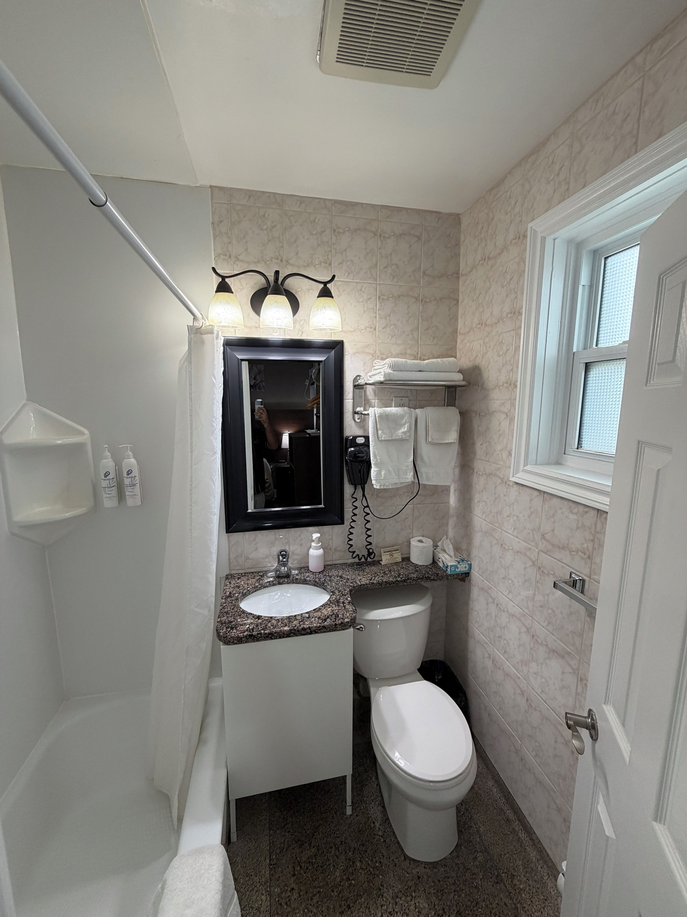 Een badkamer met een wastafel, spiegel, wastafelmeubel, toilet, handdoekhouder en een raam.