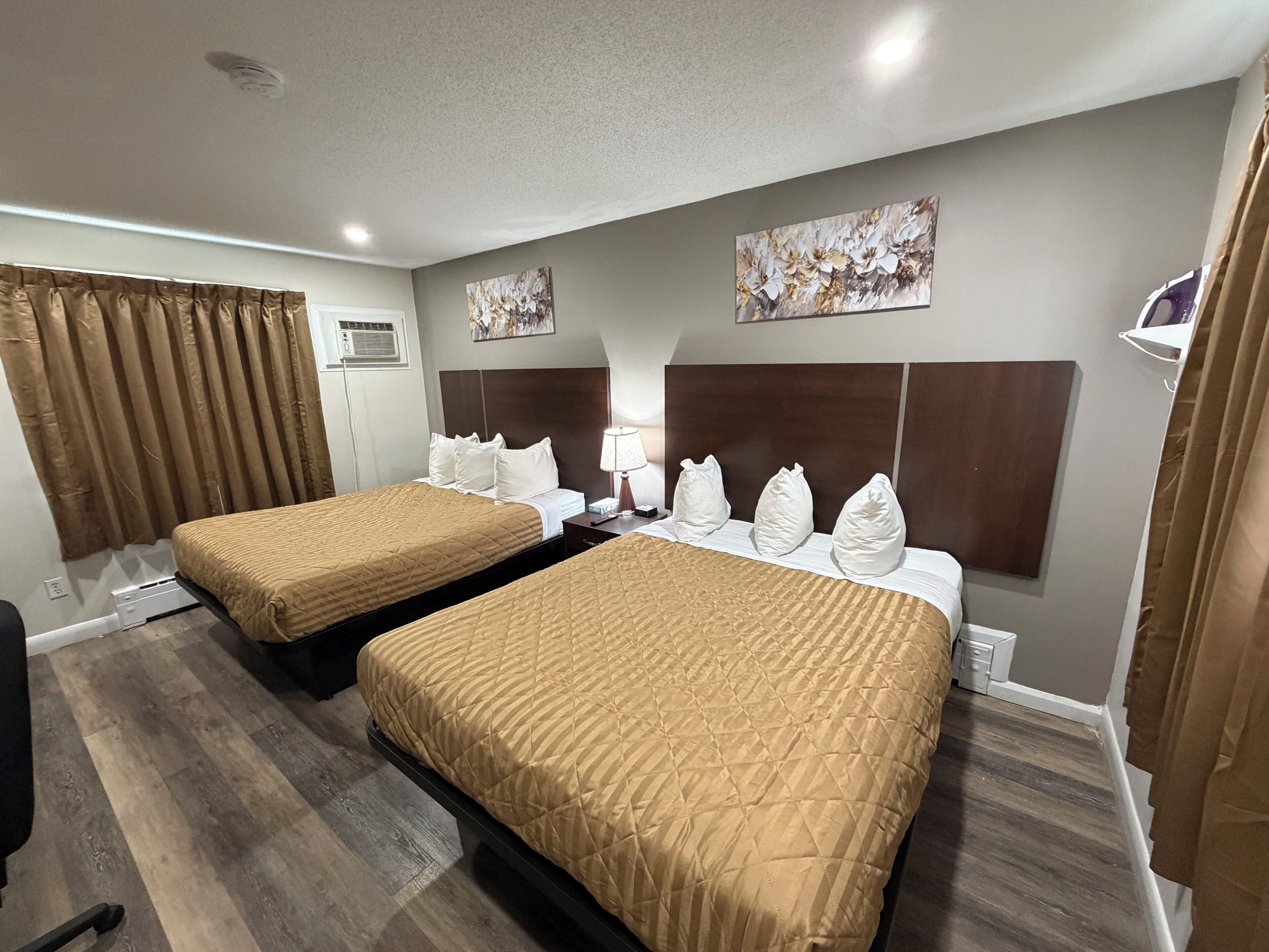 A hotel room with two beds, a headboard, a painting, and a window with curtains.