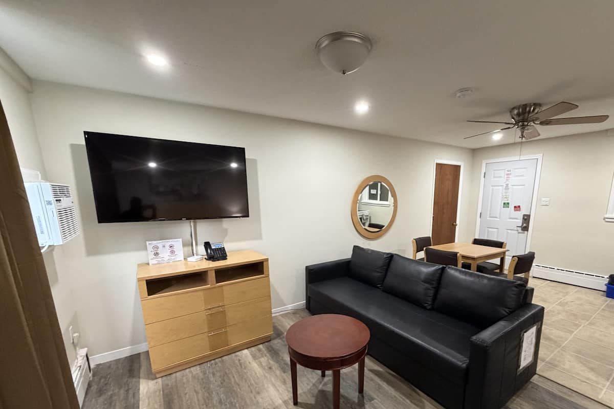 Un salon équipé d’un téléviseur à écran plat, d’un meuble en bois, d’un canapé en cuir noir, d’une table basse ronde et d’un ventilateur de plafond.