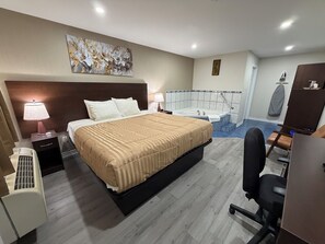 Habitación de hotel con cama, escritorio, silla, lámpara de escritorio, obra de arte en la pared, bañera y zona de ducha.