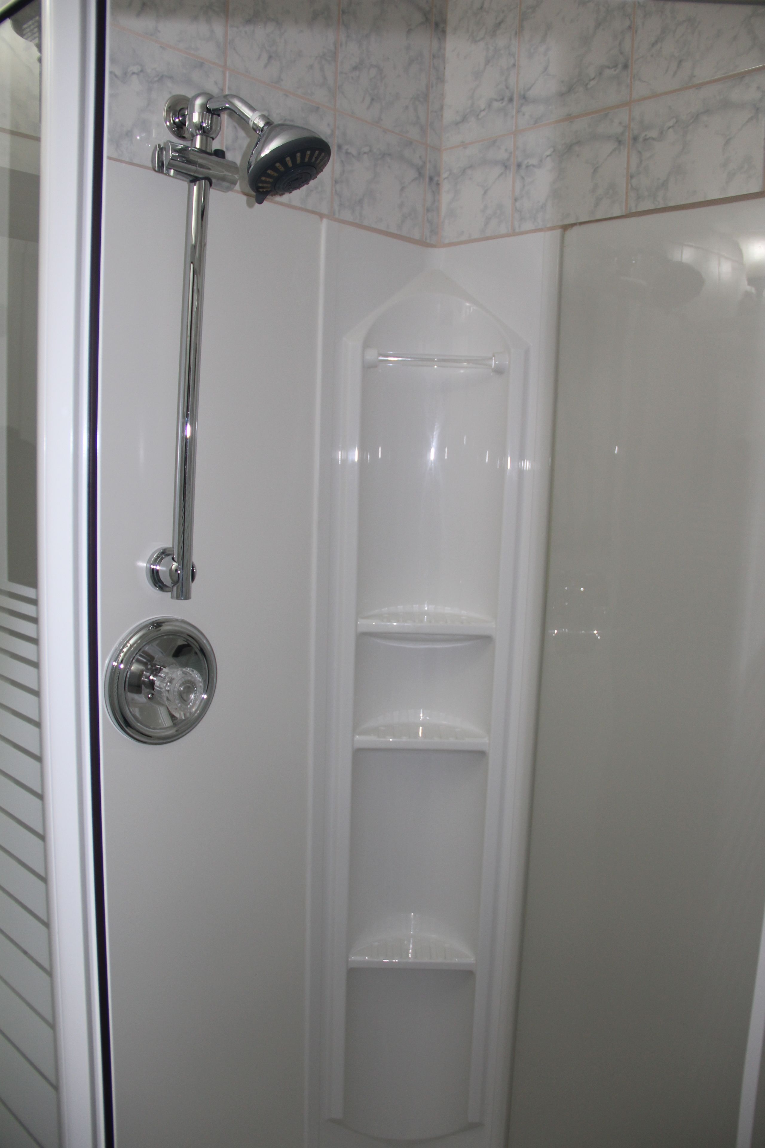 A shower with a handheld showerhead and a glass door.