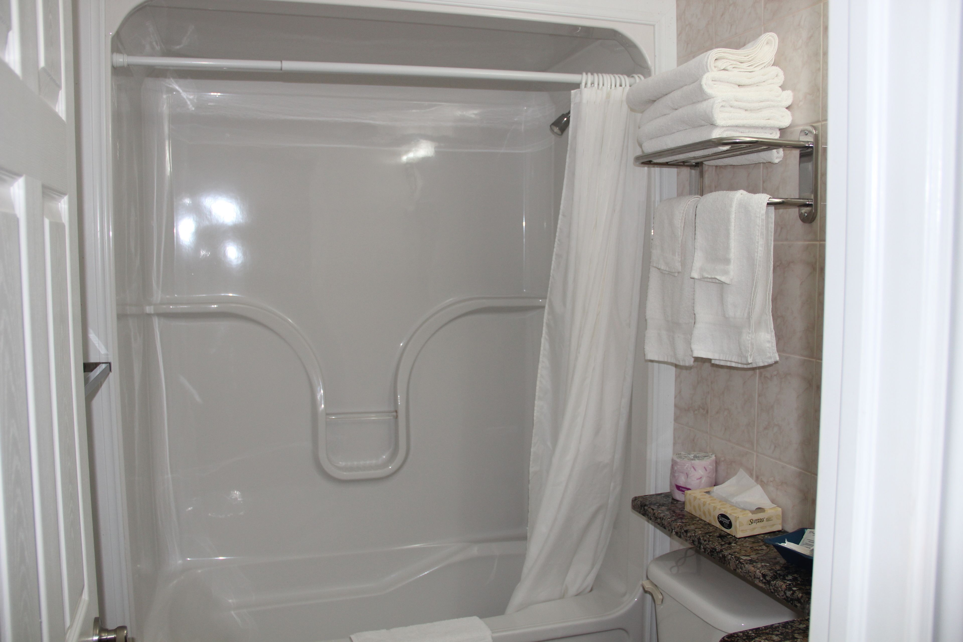 A walk-in shower with a glass door, a shower curtain, and a towel rack with folded towels.