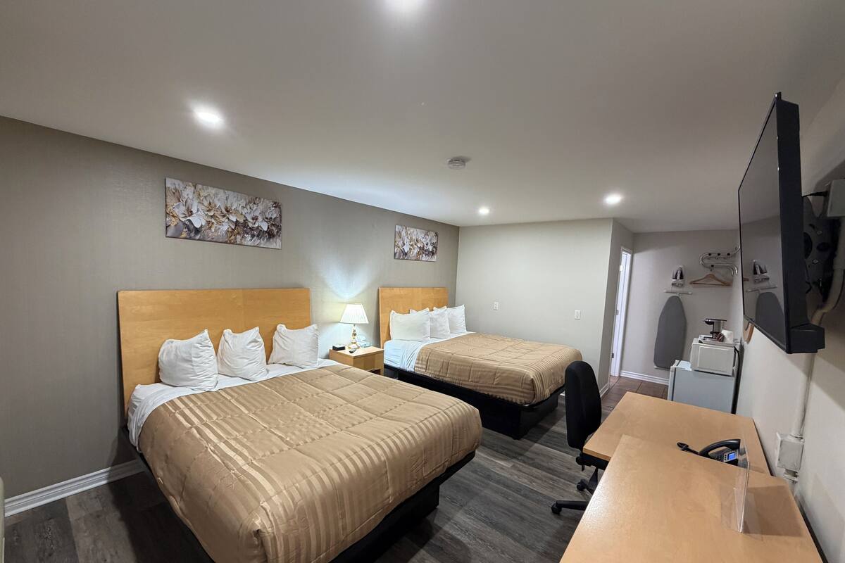 Une chambre d’hôtel avec deux lits, un bureau, une chaise, une télévision et des œuvres d’art accrochées aux murs.