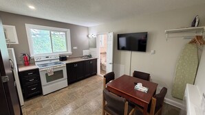 A compact kitchen with a stove, sink, and window. There's a dining table with chairs and a TV mounted on the wall. - Perth Plaza Inn & Suites (Perth)