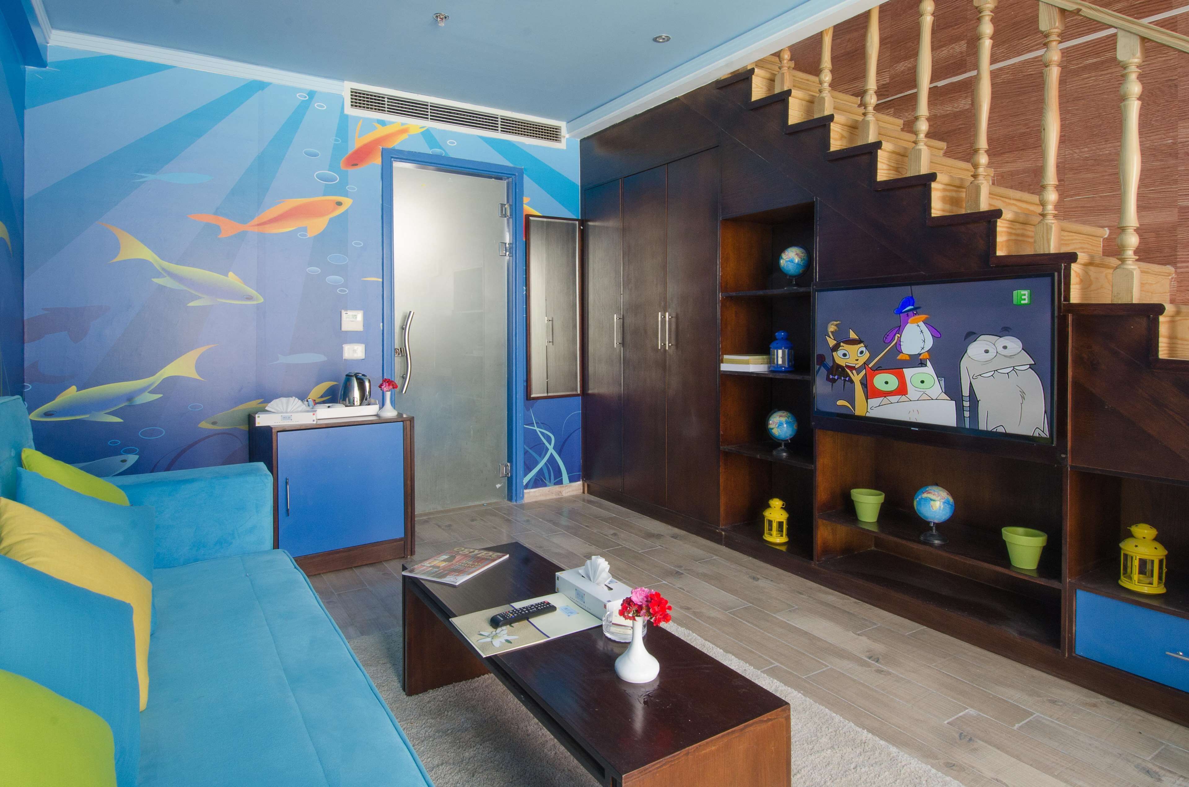 Una sala de estar con un sofá azul, una mesa de centro con un jarrón de flores, un televisor y una estantería con diversos objetos.