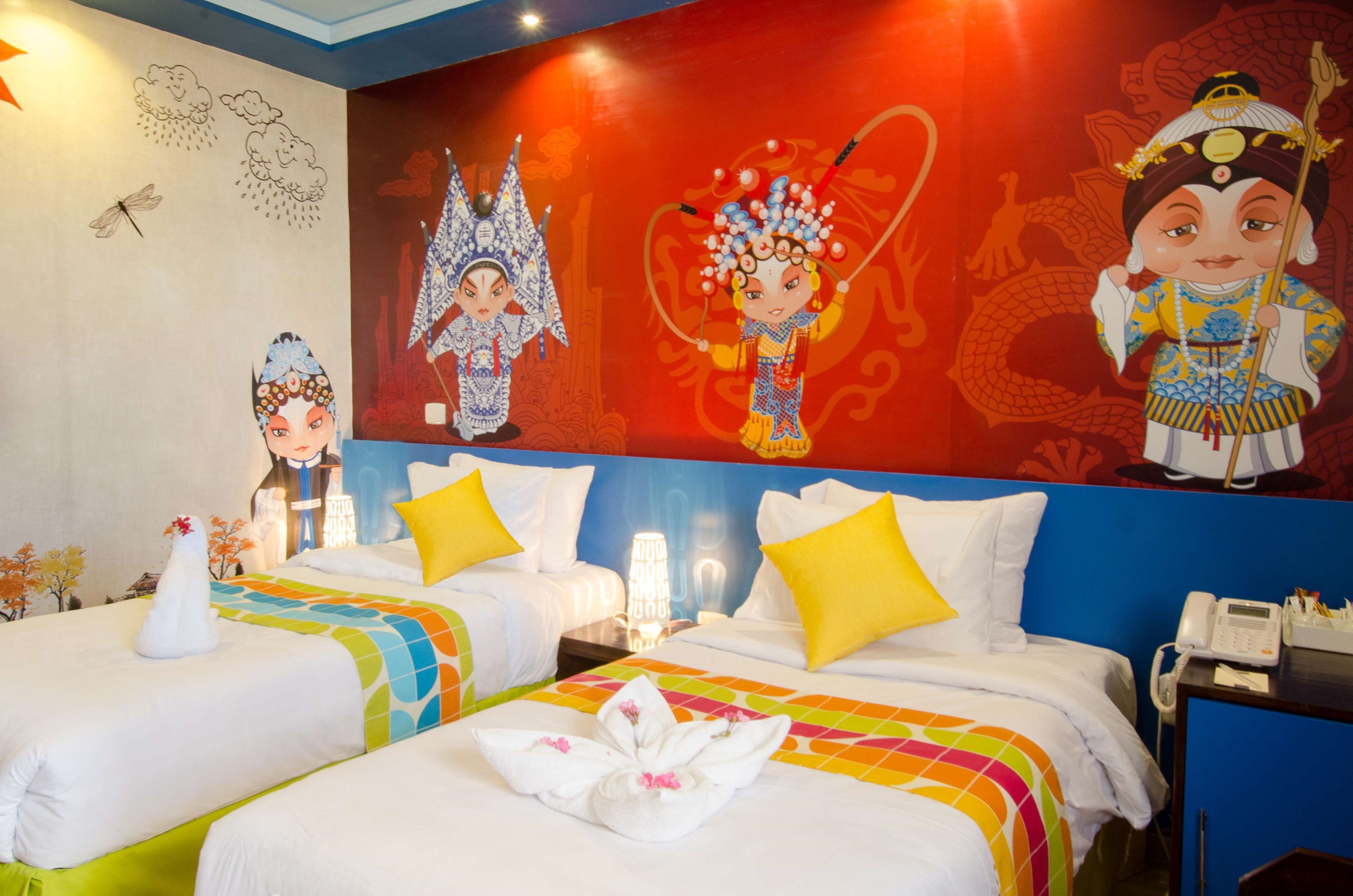A hotel room with two beds, colorful bedding, a mural with traditional figures, and a telephone on a bedside table.