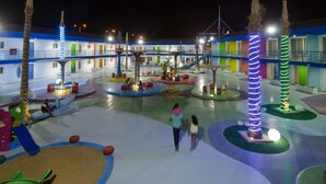 Un espacio exterior bien iluminado con edificios de colores, palmeras y una estructura de juego central.