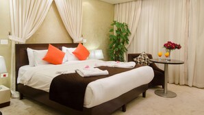 Habitación de hotel con cama, mesita de noche con un florero, lámpara y planta.