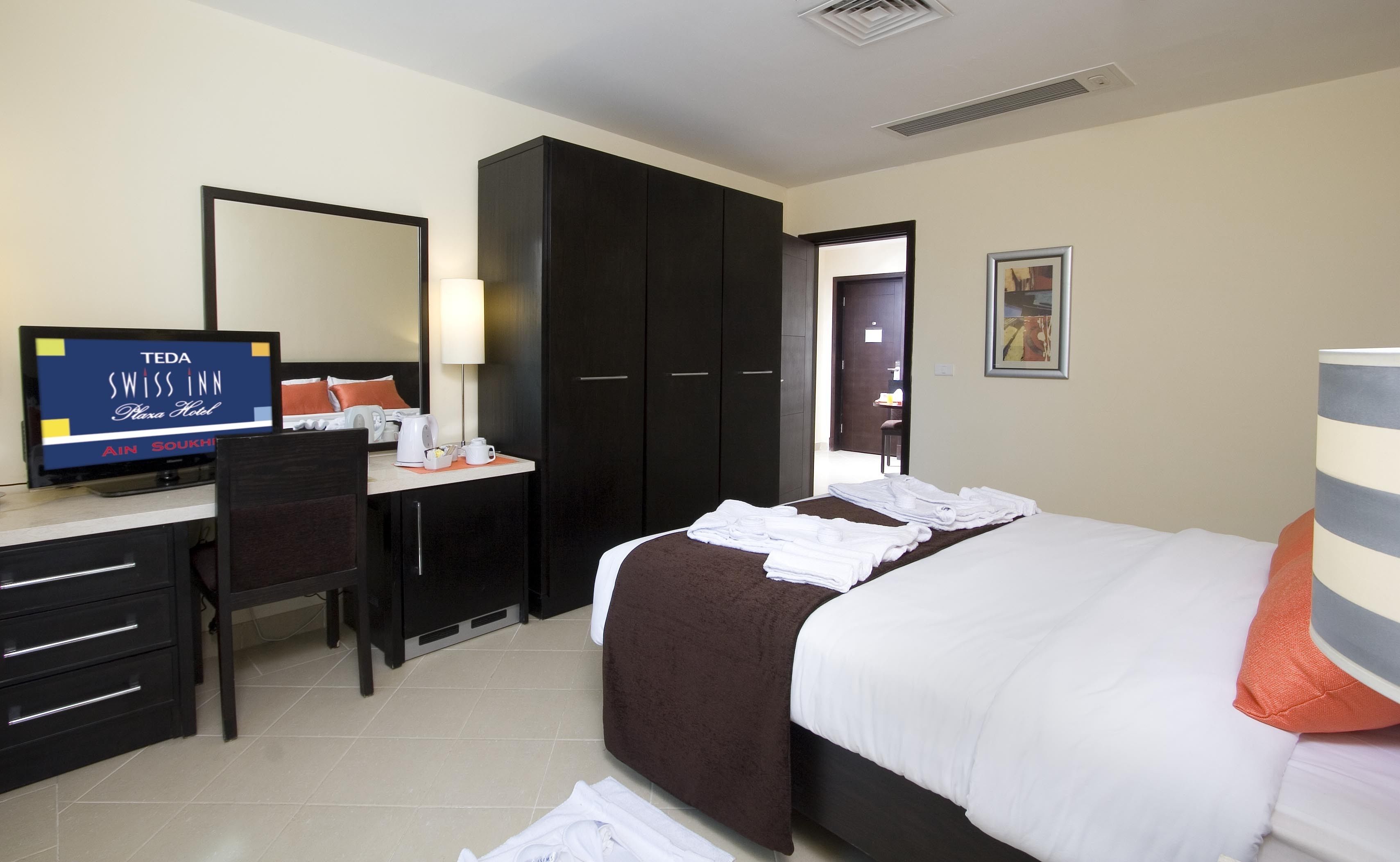 A hotel room with a bed, a desk, a chair, a TV, and a wardrobe.
