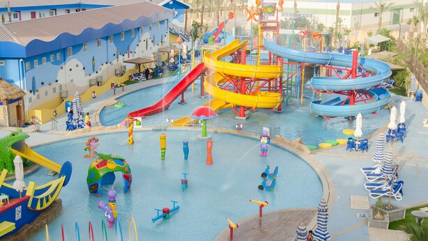 Parque acuático con múltiples toboganes y piscinas, rodeado de sillas de descanso y sombrillas.