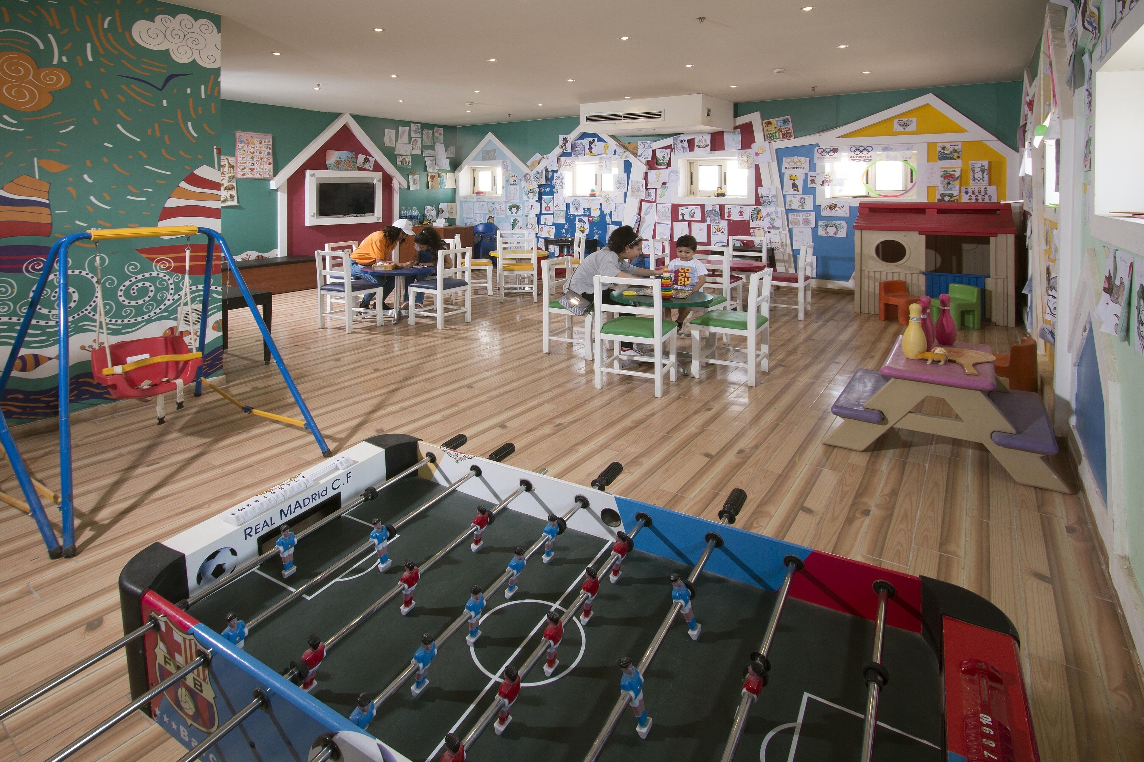 A children's play area with a foosball table, colorful murals, and various play structures.