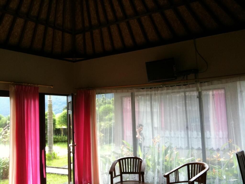 Una habitación con techo de paja, puerta corredera de vidrio y vistas al follaje exterior.