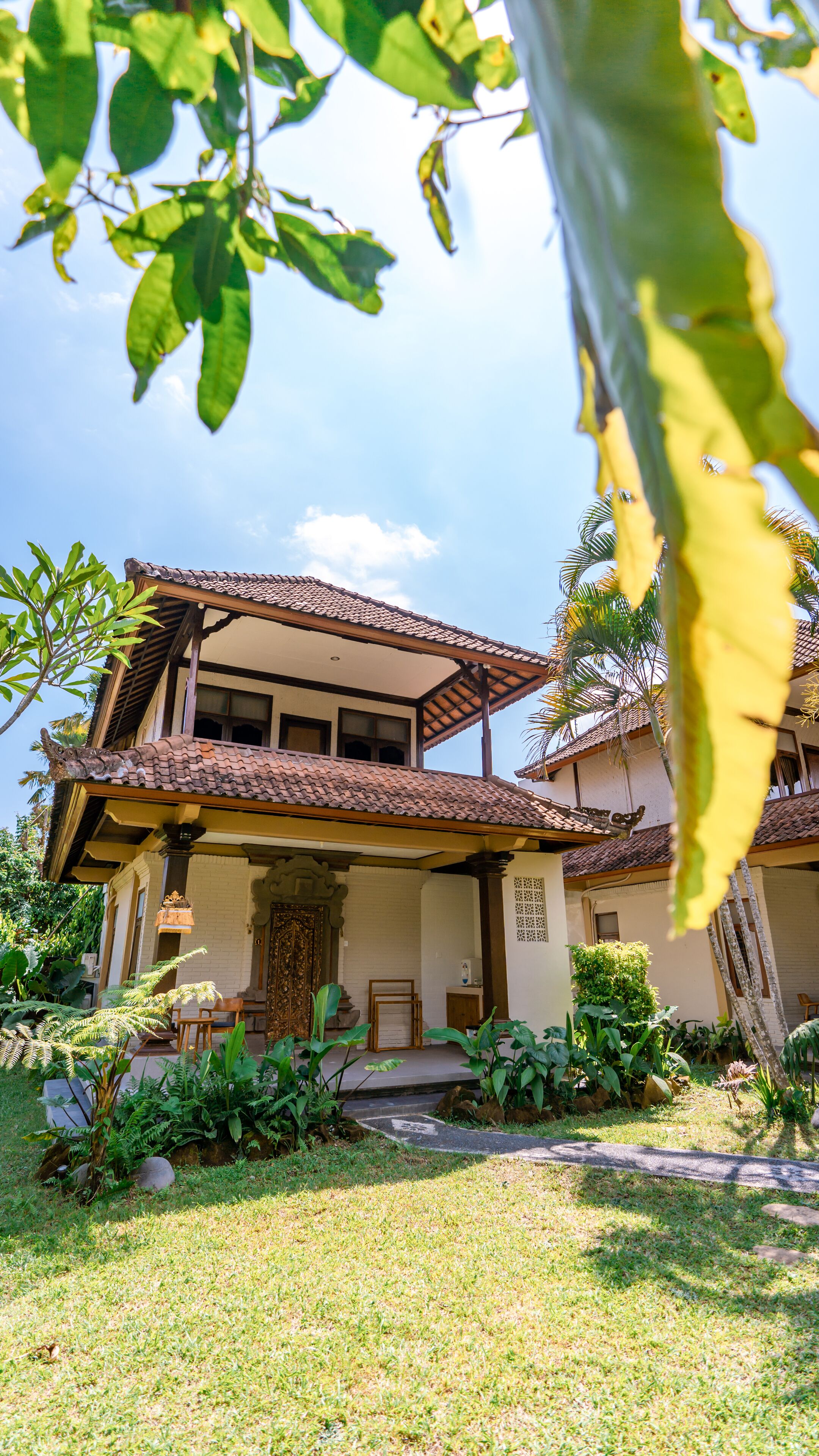 A two-story house with a tiled roof, a covered porch, and a garden with various plants.