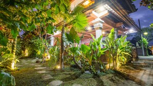 Un sendero bien iluminado en un jardín que conduce a un edificio tradicional con techo de madera y columnas.