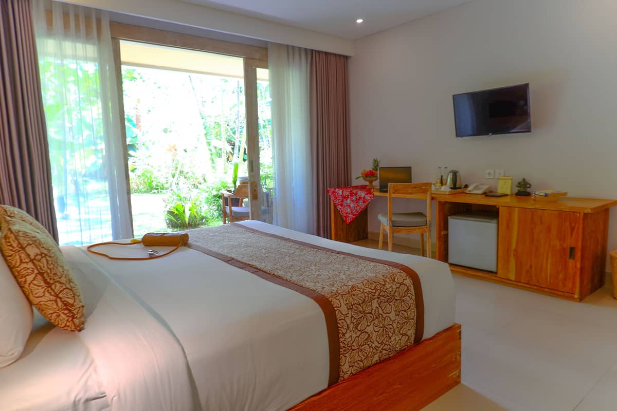 Quarto de hotel com cama grande, escrivaninha, televisão e vista para o verde lá fora.