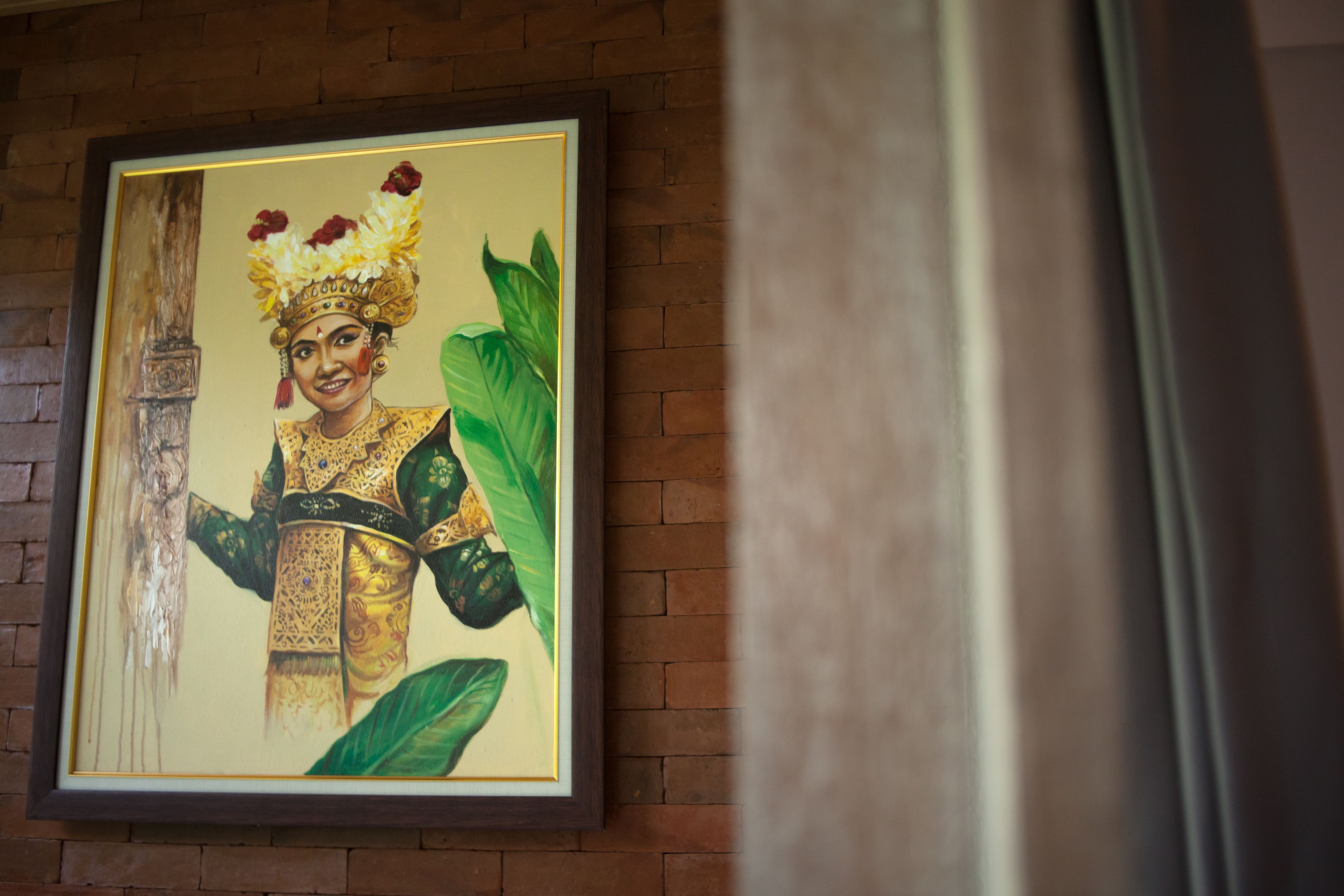 A framed painting of a figure in traditional attire on a brick wall.