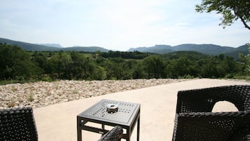 An outdoor seating area with wicker chairs and a metal table, overlooking a mountainous landscape.