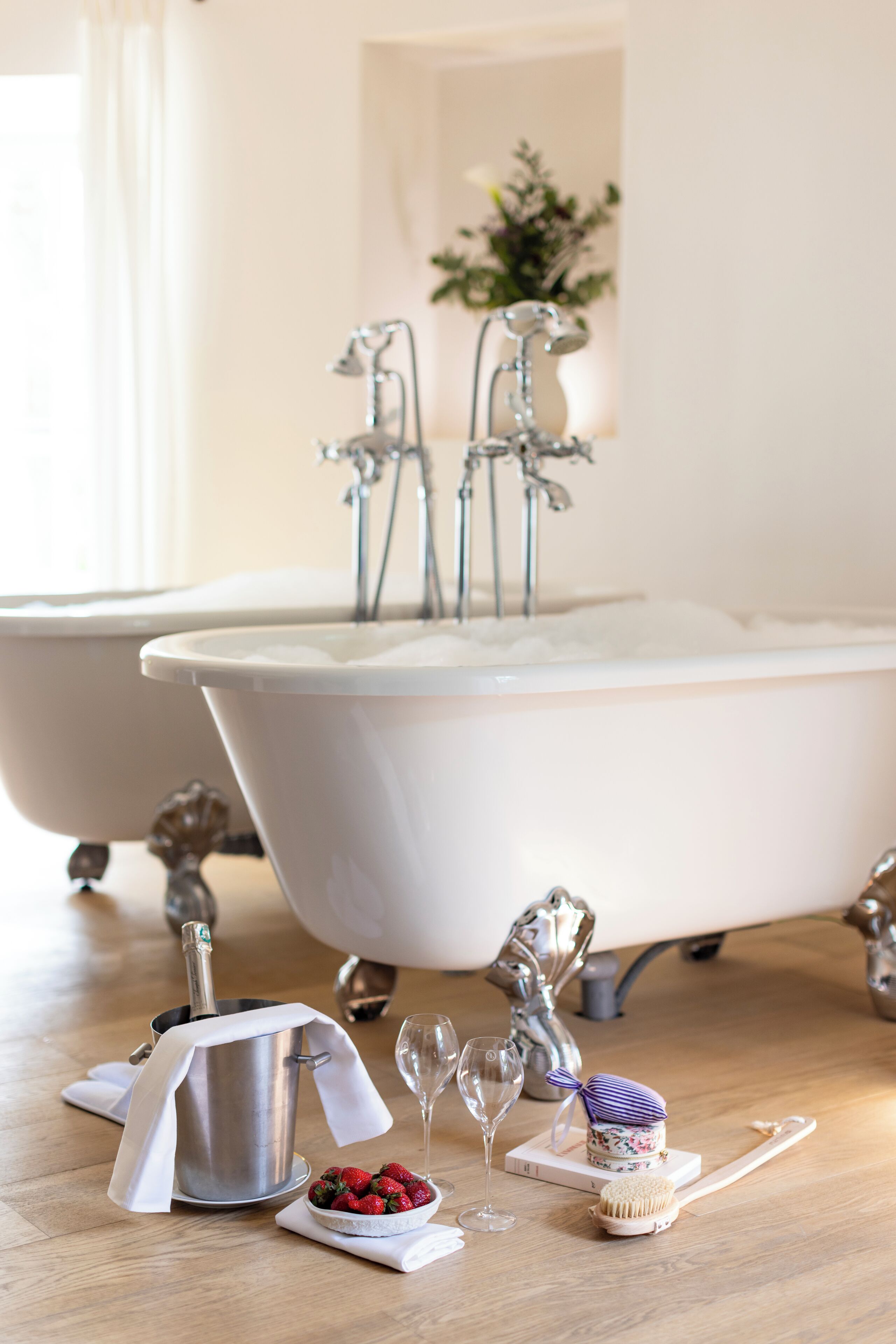 Une salle de bain avec une baignoire blanche, une bouteille de champagne, des fraises, un verre à vin et une brosse à dents.
