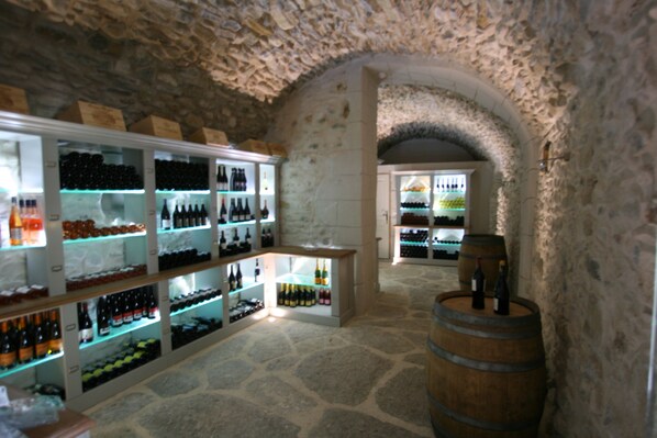 Una bodega con estantes llenos de botellas, un barril de madera y paredes de piedra.
