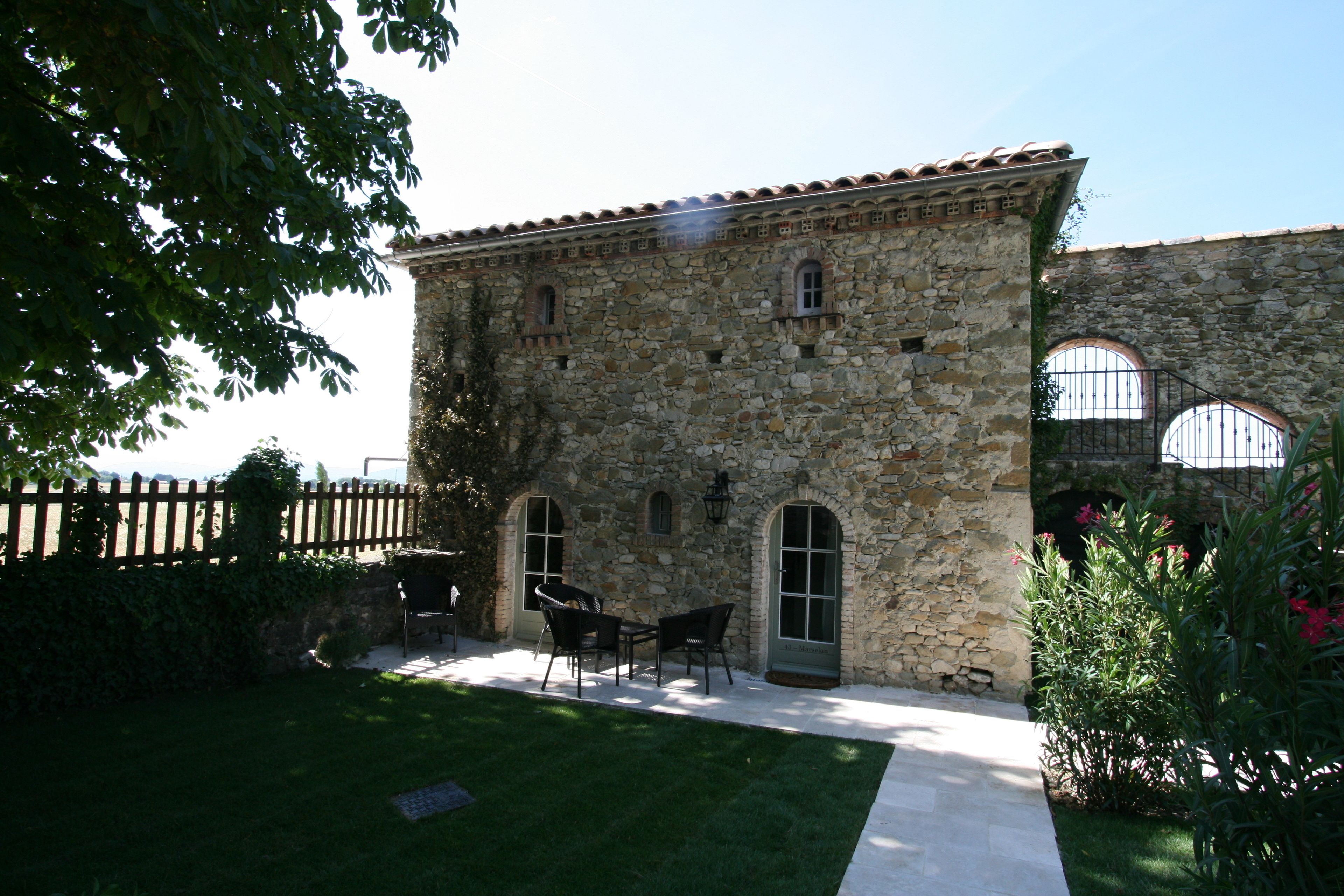Un edificio de piedra con techo de tejas, un patio empedrado y mobiliario de exterior.