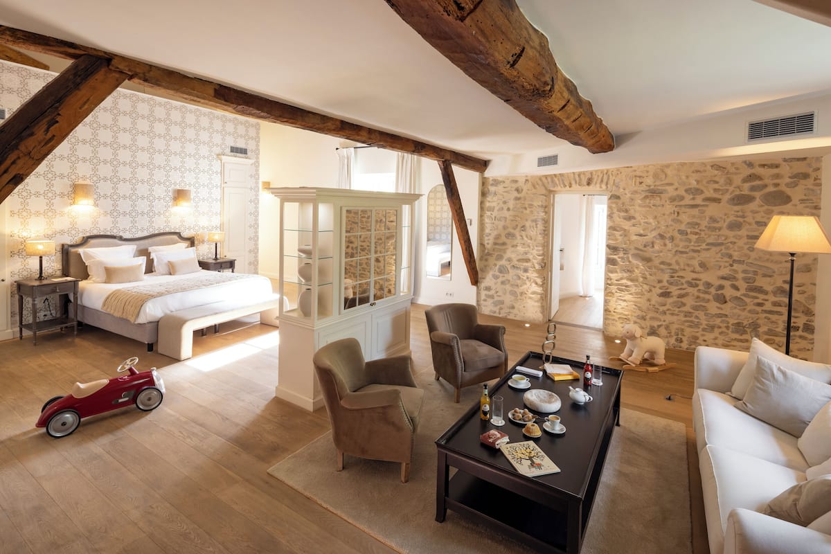 A spacious room with a large bed, a wooden ceiling, stone walls, and a dining area with a table and chairs.