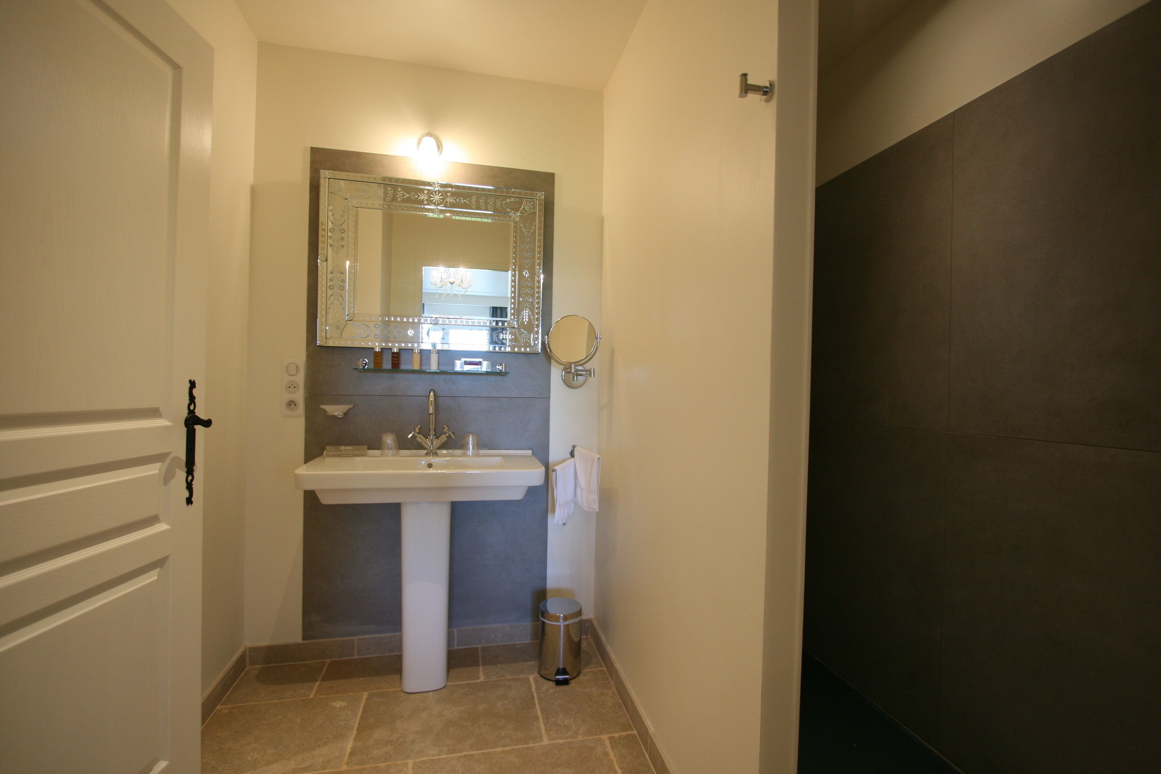 A bathroom with a pedestal sink, a large mirror, a towel rack, and a trash can.