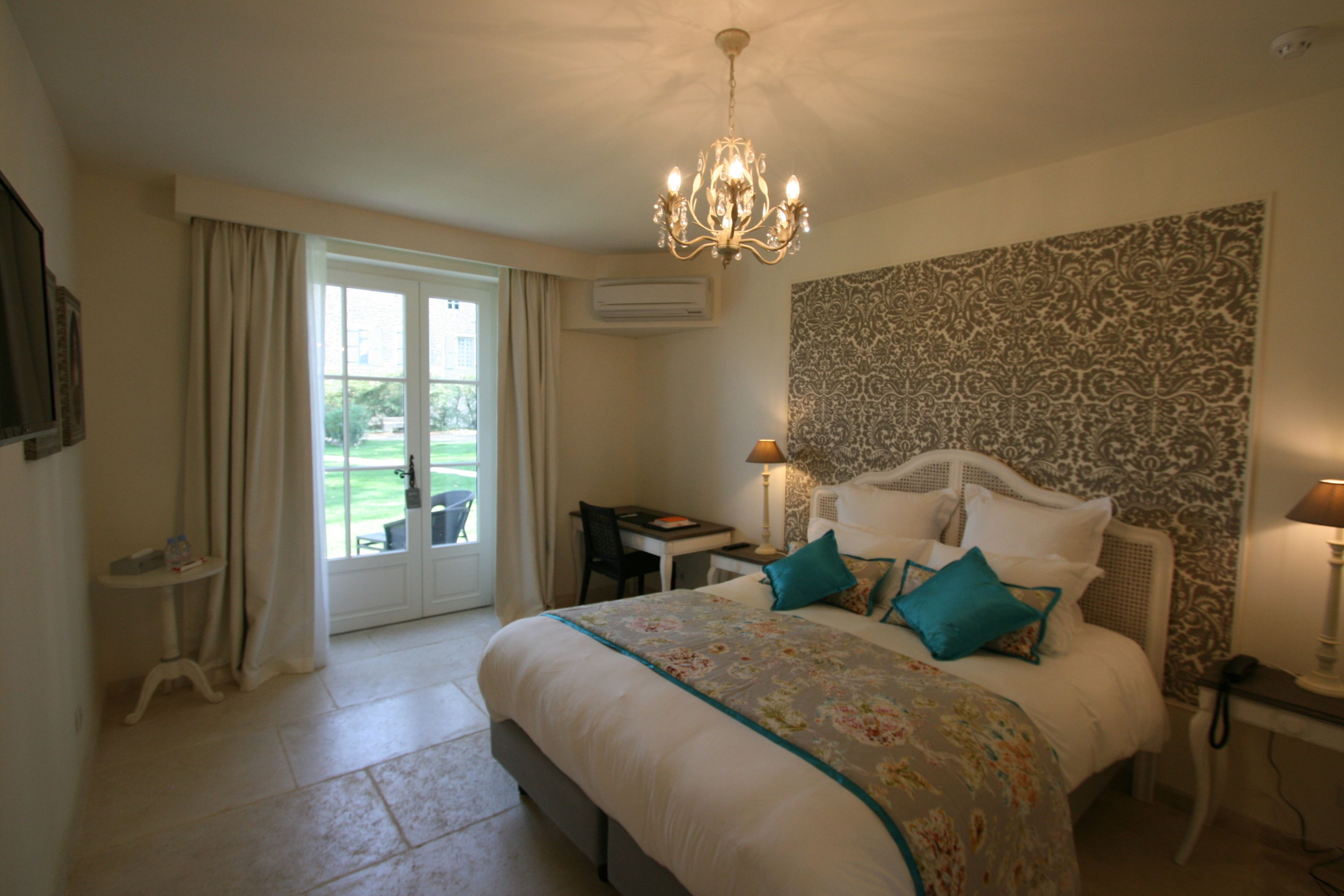Quarto com cama grande, lustre, escrivaninha e vista para o exterior.