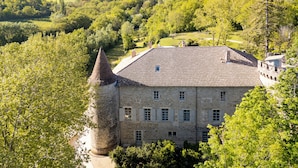 A stone building with a conical tower, surrounded by lush greenery and hills in the background.