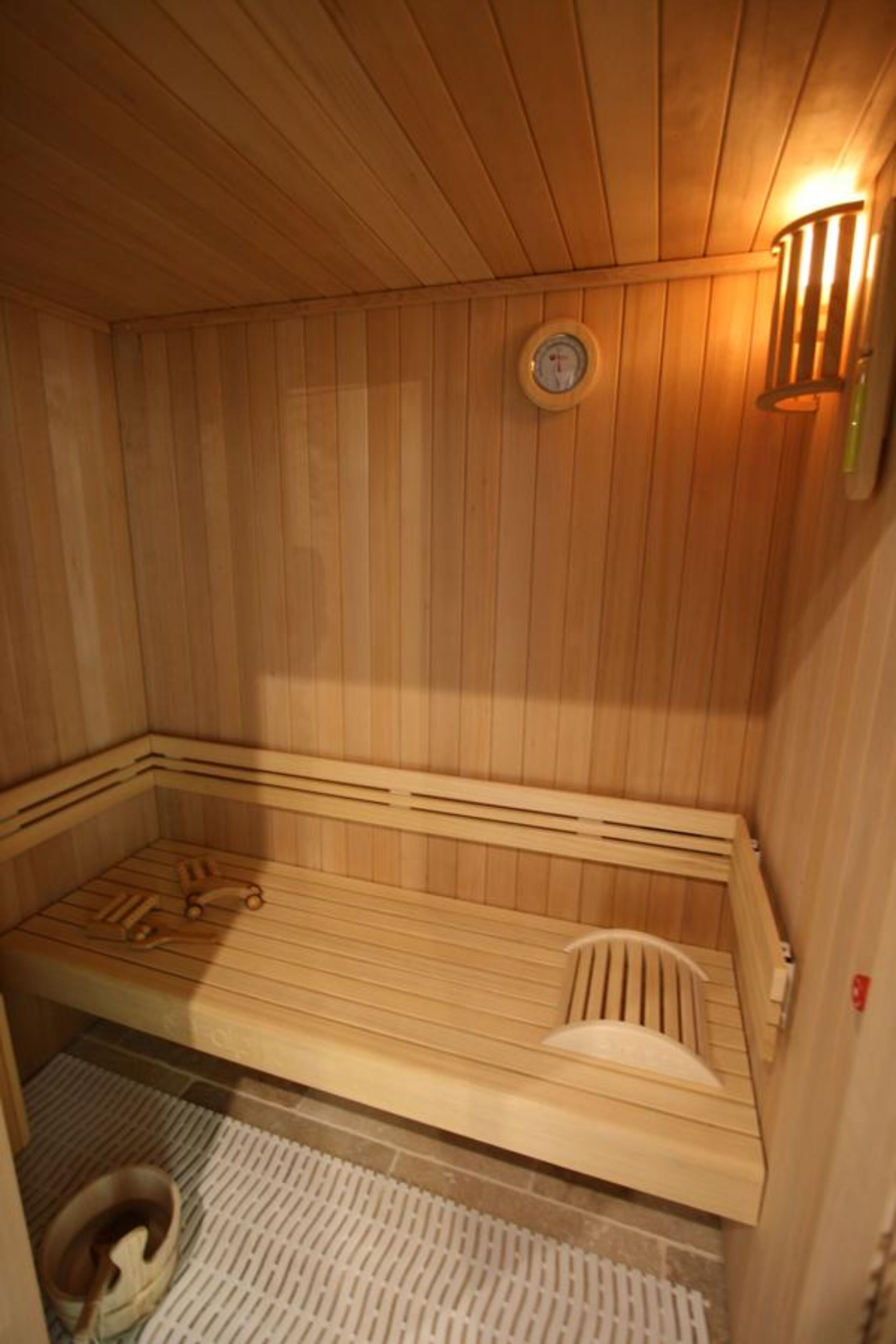 A wooden sauna with benches, a wall-mounted clock, and a light fixture.