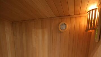 A wooden sauna with benches, a wall-mounted clock, and a light fixture.