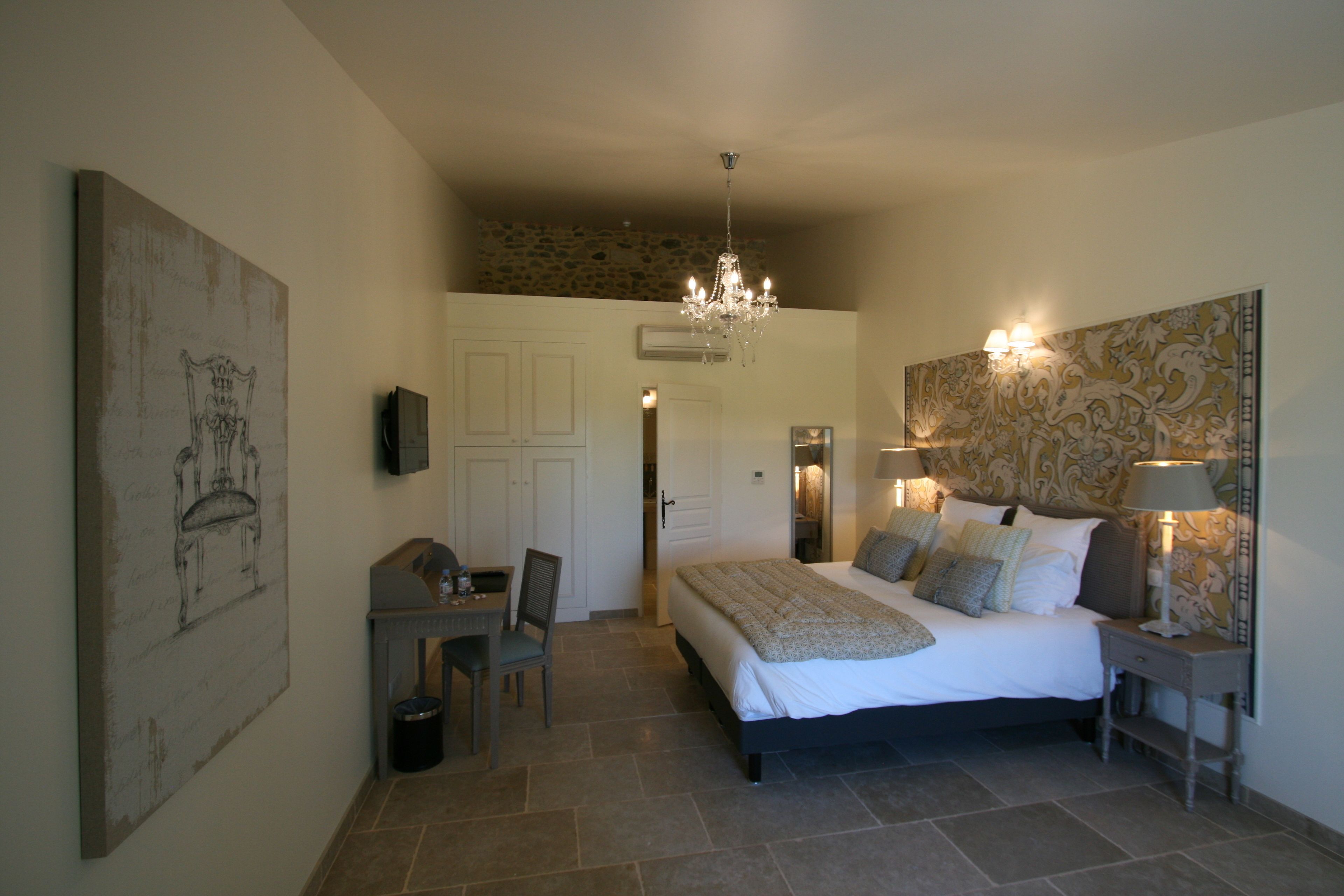 A bedroom with a large bed, bedside lamps, a desk with a chair, and a chandelier.