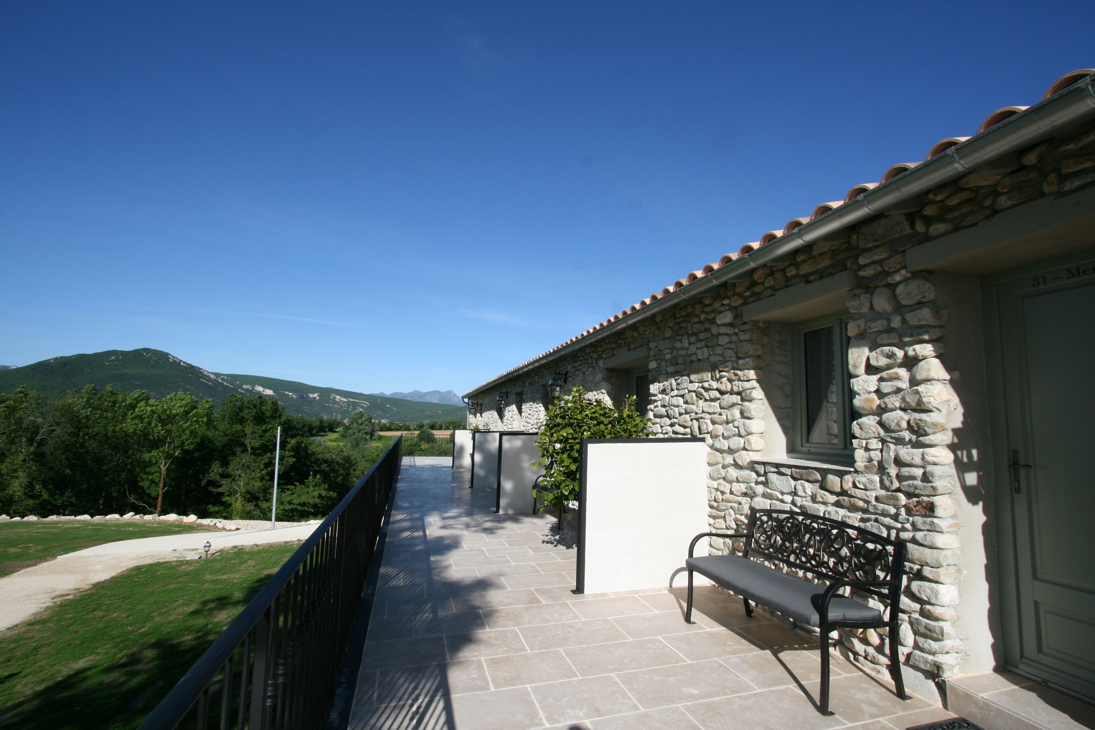 Un bâtiment en pierre doté d’un balcon, d’un banc et offrant une vue sur les montagnes.